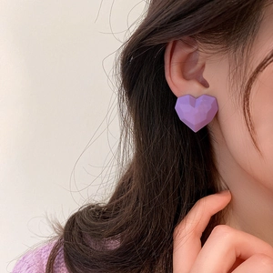 Macro view of purple geometric heart stud earrings worn by a model in soft light