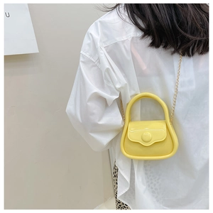 Close-up of yellow jelly mini chain bag worn by a model against a white background