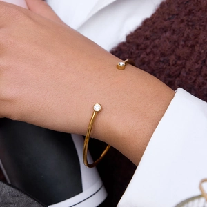 Elegante vergulde open armband met twee zirkoonstenen om een pols gedragen