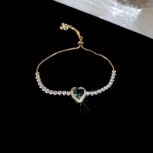 Detail of a gold heart-shaped bracelet with green zircon and adjustable slider clasp
