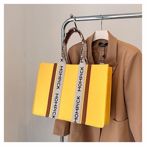 Detail of a yellow felt tote bag with letter print straps and a camel suit background