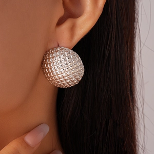 Close-up of a silver spherical stud earring with geometric grid texture on model ear