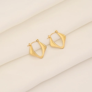 Close-up of golden geometric twisted rhombus earrings on white silk fabric background