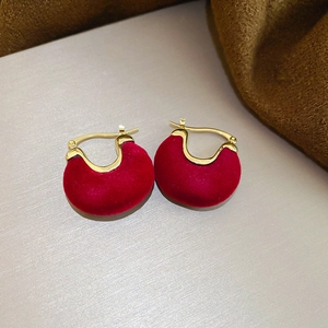 Detailed close-up of red velvet C-shaped earrings with gold metal fasteners on fabric