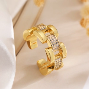 Détail macro d'une bague chaîne dorée avec pavé de zircons sur fond de soie douce