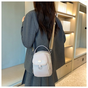 Detail of multi-layered beige nylon crossbody bag with metal ring shown on model
