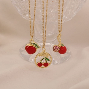 Three gold necklaces with cherry and strawberry pendants on a luxury crystal glass