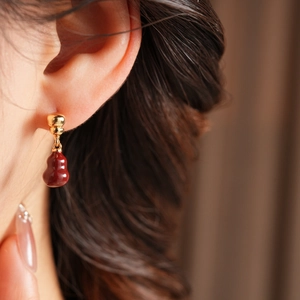 Close-up of 18k gold plated earrings featuring red gourd pendants on a model