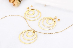 Close-up of golden concentric circle pendant necklace and stud earrings set on white surface