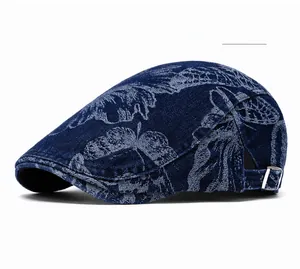 Detail of deep blue denim beret featuring white leaf pattern and adjustable side metal buckle
