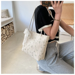 Detail of hand-woven straw tote bag with green floral embroidery and white lace bow decoration