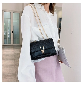 Detail of black quilted crossbody bag with golden chain strap and unique U-shaped lock closure