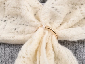 Detail of white hollow lace fabric with gold metal ring on grey knitwear sweater