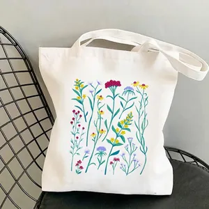 Minimalist white wildflower garden canvas tote bag shown on a mesh metal chair