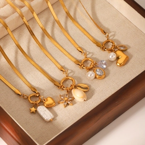 Three gold plated stainless steel blade chain necklaces with pearls and charms on a wood tray