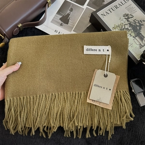 Detail of olive green fringe scarf with woven label and premium texture on flat lay