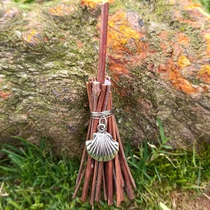 Close-up of a mini witch broom pendant with silver shell charm on natural mossy bark
