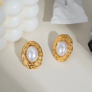 Detail of oval golden earrings with large pearl inlay on textured metal background