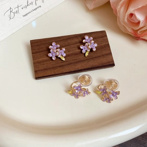 Detailed comparison of purple enamel flower stud and clip-on earrings on ceramic tray