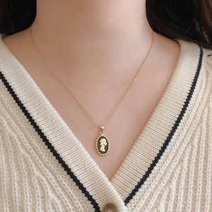 Detail of a gold necklace with a black cameo oval queen pendant worn by a female model