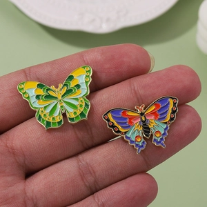 Set of two colorful butterfly enamel pins in purple and yellow on a green background