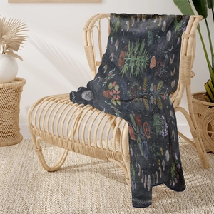 Detail view of dark grey flannel blanket with floral moon phase patterns on a rattan chair