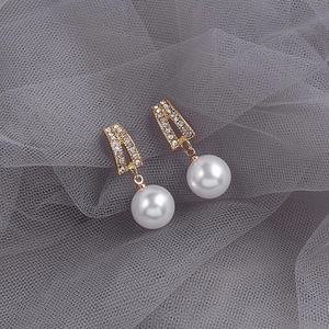 Close-up of gold pearl earrings with white cubic zirconia on a gray mesh background
