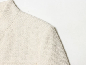 Detailed macro view of off-white tweed texture and shoulder stitching on a jacket