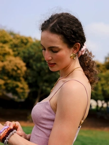 Close-up of golden textured square earrings and satin hair scrunchies on a model