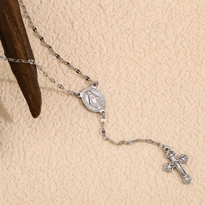 Detailed view of silver rosary necklace with virgin mary medal and cross pendant on branch