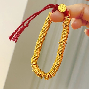 Detail of beaded bracelet with red cord featuring a gold charm engraved with Fu character
