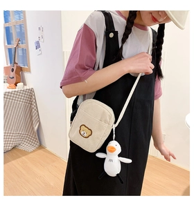 Detail of cute bear embroidery and duck charm on corduroy mini crossbody bag