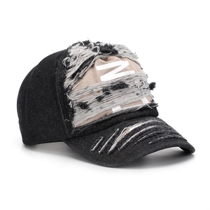 Detail of distressed black denim baseball cap with beige 'N' patch and frayed edges