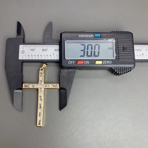 Macro shot measuring the 30mm width of a gold cross pendant with cubic zirconia stones