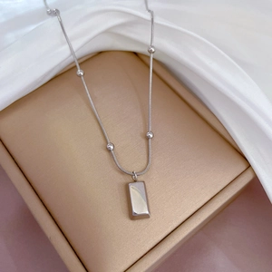 Detailed view of silver snake chain necklace with rectangular pendant on silk
