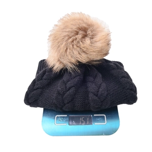 Gorro de punto negro de invierno con pompón de piel, pesando 151g en una báscula.