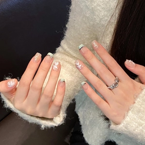 Detailed view of handmade mint green nails with hand-painted white flowers and rhinestones
