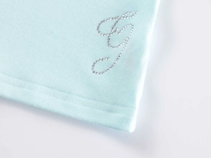 Detailed macro view of light blue ribbed fabric featuring a sparkling rhinestone G letter
