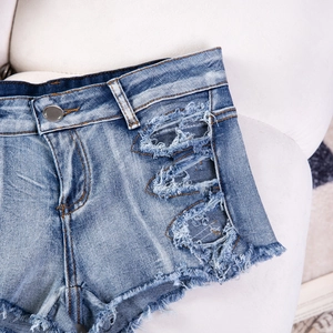 Dettaglio di pantaloncini di jeans blu con strappi usurati e trama lavata