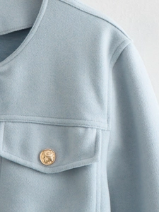 Close-up of light blue tweed jacket featuring a gold embossed button and flap pocket