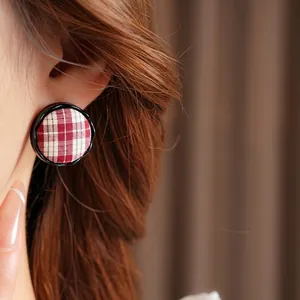 Elegant round red plaid fabric earrings with black metal frames worn by a model