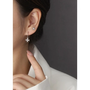 Close-up of sparkling S925 silver cross star stud earrings worn on a model's ear