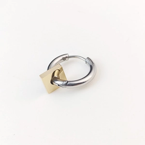 Macro shot of silver metal hoop earring featuring a geometric gold square pendant charm