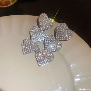 Close-up of sparkling heart-shaped stud earrings with crystals on a white ceramic plate
