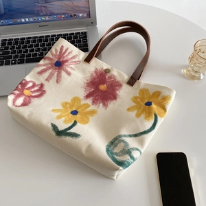 Detailed view of floral canvas tote bag with brown leather handles on a white desk