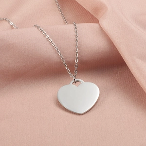 Detailed view of silver heart pendant necklace on soft pink fabric folds backdrop
