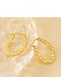 Close-up of gold-plated oval earrings with hammered texture on beige silk background