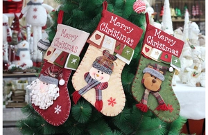 Drei bestickte Weihnachtssocken in Rot, Beige und Grün hängen an einem festlichen Baum