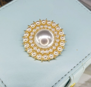 Détail d'une broche vintage en perles avec base dorée sur une boîte à bijoux bleue