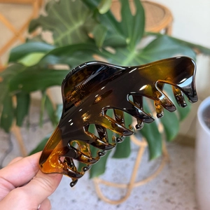 Detailed view of amber textured claw clip held by hand with a soft garden background